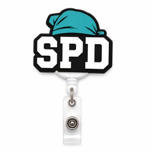 Op de afbeelding: Een badgehouder met een zwart-wit afbeelding met de letters SPD in een vetgedrukt lettertype. Boven de letters staat een turquoise muts. De badgehouder heeft een witte kunststof behuizing en een doorzichtig plastic bandje met een metalen knop.