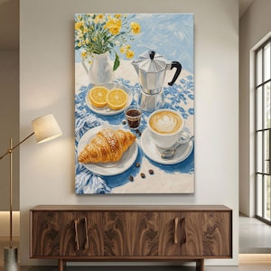 May include: A vertical canvas painting depicting a breakfast scene on a blue and white patterned tablecloth. It features a white pitcher with yellow flowers, a silver moka pot, two orange slices, a croissant on a plate, and a cup of latte.