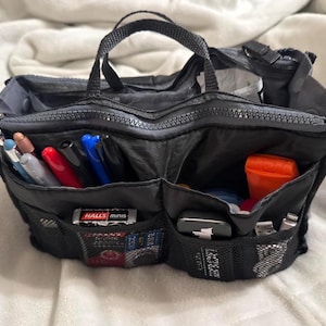 May include: Black nylon purse organizer with multiple compartments and a zipper closure. The organizer has a handle and contains pens, a small orange container, and a package of Halls Minis.