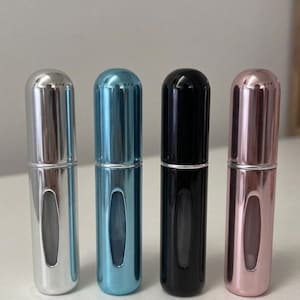 May include: Four small, refillable perfume atomizers in a row. The atomizers have a cylindrical shape with a metallic finish. Colors include silver, teal, black, and rose gold. Each atomizer has a clear window to view the contents.