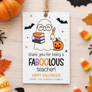 May include: A rectangular white gift tag with a lined paper pattern featuring a cartoon ghost wearing glasses, holding a stack of three books and a yellow pencil next to a jack-o'-lantern. Text reads: thank you for being a FABOOLOUS teacher! HAPPY HALLOWEEN! FROM: THE SOPHIA'S FAMILY.