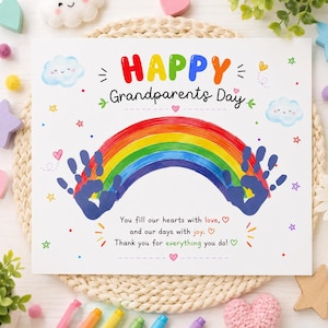 Może przedstawiać: Biała prostokątna kartka z napisem HAPPY Grandparents Day kolorowymi literami, namalowaną tęczą i dwoma niebieskimi odciskami dłoni. Pod tęczą znajduje się tekst: You fill our hearts with love, and our days with joy. Thank you for everything you do!