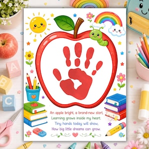 May include: A white rectangular art print featuring a large red apple outline containing a red handprint. The print includes a smiling sun, a green caterpillar, a rainbow, and a stack of books. Text reads: An apple bright, a brand-new start, Learning grows inside my heart. Tiny hands today will show, How big little dreams can grow.