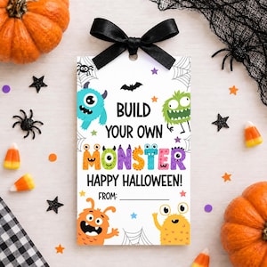 Può includere: Un'etichetta regalo rettangolare bianca con un fiocco di nastro di raso nero sulla parte superiore. L'etichetta mostra mostri colorati dei cartoni animati, ragnatele, stelle e il testo "BUILD YOUR OWN MONSTER HAPPY HALLOWEEN!".