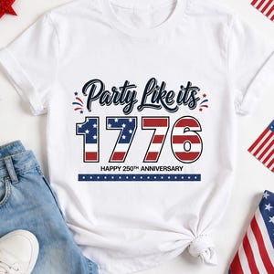 Pode incluir: Camiseta branca com a frase "Party Like its 1776" em azul marinho e vermelho, celebrando o 250º aniversário. O design inclui estrelas e listras, com calções de ganga e ténis brancos.