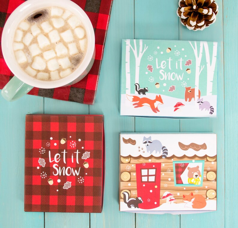 以下が含まれることがあります： 「Let it Snow」と書かれた赤と黒の格子縞のギフトボックスが2つ。1つのボックスには、キツネ、アライグマ、クマが描かれた冬のシーンが描かれている。もう1つのボックスには、屋根にアライグマ、窓にクマがいる小屋が描かれている。