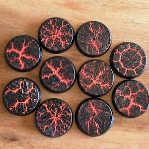 Peut inclure: Neuf socles circulaires pour figurines présentant une surface noire texturée avec des fissures rouges éclatantes rappelant de la lave. Chaque socle possède un bord surélevé et un motif distinct de craquelures, créant un aspect volcanique.