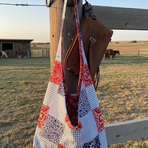 Può includere: Una borsa a tracolla stile hobo realizzata con un patchwork di quadrati di tessuto rosso, bianco e blu. Il motivo presenta un mix di stampe bandana paisley tradizionali e piccoli quadretti vichy con una lunga tracolla annodata in alto.