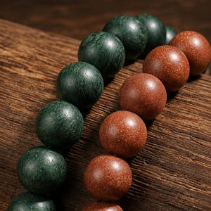 May include: Two strands of spherical beads arranged in parallel lines. One strand consists of dark green, textured, matte-finish beads, while the other strand features shimmering, reddish-brown, glittery beads with a smooth, polished surface.