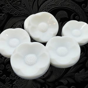 May include: A set of five white ceramic objects shaped like five-petaled flowers. Each piece features a smooth, rounded outer edge and a textured, circular center with a dotted surface, resembling the stamen of a blooming flower.