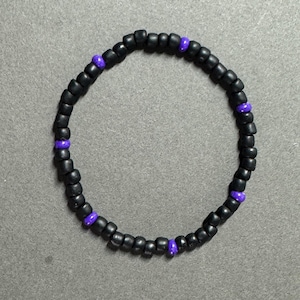 May include: A black beaded bracelet with purple accent beads. The bracelet is circular and made of small, round beads. The purple beads are evenly spaced around the bracelet.