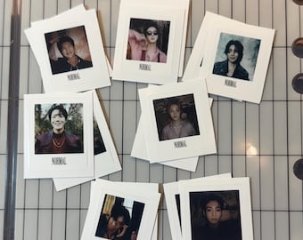 Puede incluir: Una colección de siete impresiones fotográficas cuadradas blancas con retratos individuales, cada una con la palabra NORMAL impresa en negro en la parte inferior. Las impresiones están dispuestas sobre una superficie de cuadrícula marcada en cm.