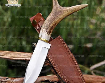 May include: A fixed-blade knife with a polished silver steel blade and a textured brown antler handle. The knife features a brass bolster and is accompanied by a brown leather sheath with decorative stitching and a metal snap button closure.