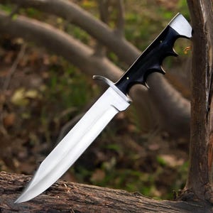 May include: A fixed-blade knife featuring a polished silver-toned steel blade with a prominent central ridge and a sharp point. The handle is crafted from smooth black material with a contoured finger-grooved grip and a silver-toned metal guard.