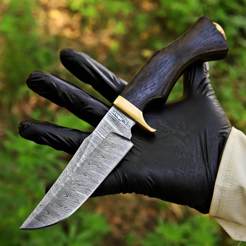 May include: A fixed-blade knife featuring a patterned Damascus steel blade, a dark brown wooden handle with a visible grain, and a polished brass bolster. The blade displays a distinct wavy, layered metal texture throughout its surface.