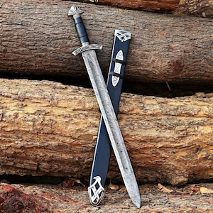 May include: A double-edged sword with a patterned Damascus steel blade, a black grip, and a silver crossguard. The sword is paired with a black scabbard featuring silver metal accents, including a decorative eagle emblem at the bottom tip.