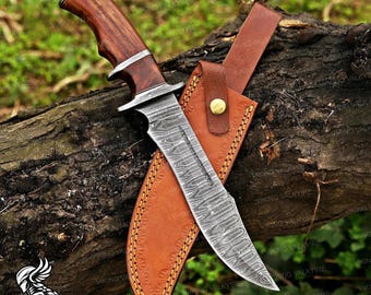 May include: A fixed-blade knife with a patterned Damascus steel blade and a polished dark wood handle featuring silver-toned metal bolsters. The knife is accompanied by a tan leather sheath with visible stitching and a brass-colored snap button.