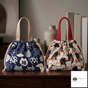 Pode incluir: Duas bolsas com cordão e alças. A bolsa da esquerda é azul-marinho com padrões de gatos brancos e o caractere japonês para gato. A bolsa da direita apresenta um padrão multicolorido de gatos da sorte com uma alça vermelha sólida.