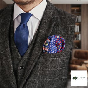 Op de afbeelding: Een donkergrijs vest met een vensterruitpatroon gedragen over een wit overhemd met een effen marineblauwe stropdas. Een felblauw pochet met een veelkleurig paisley- en geometrisch bloemenpatroon zit in de borstzak van het kledingstuk.