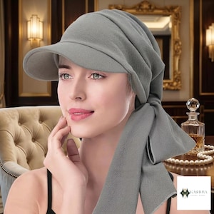 Peut inclure: Un couvre-chef gris uni doté d'une visière structurée et d'un long pan de tissu drapé qui se noue sur le côté. Le matériau présente une texture fine et subtile sur toute la surface, offrant un aspect uniforme à l'ensemble de l'accessoire.
