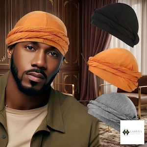 Könnte beinhalten: Eine Kollektion von drei Kopftüchern in Schwarz, Orange und Grau. Jedes Kopftuch verfügt über eine glatte, abgerundete Krone und ein breites, strukturiertes, gedrehtes Band, das die Basis umschließt. Der Stoff wirkt weich und leicht und ist so konzipiert, dass er eng am Kopf anliegt, mit einer geschichteten, gerafften Optik an der Vorderseite.