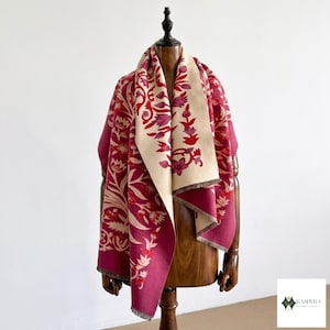 Peut inclure: Un châle réversible présentant une palette de couleurs magenta profond et crème avec un motif floral répétitif. Le tissu affiche des motifs botaniques complexes dans des tons de rouge et rose foncé, fini avec un ourlet simple sur les bords.
