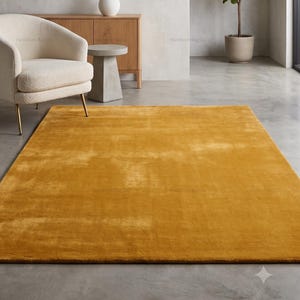 May include: A rectangular area rug in a solid, vibrant mustard yellow color with a soft, plush texture. The rug features a consistent, uniform pile throughout its surface, providing a smooth and even appearance across the entire floor covering.
