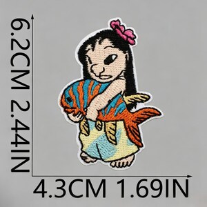 May include: An embroidered patch featuring a character with black hair and a pink flower, holding an orange and blue striped fish. The patch measures 6.2 cm by 4.3 cm, which is equivalent to 2.44 inches by 1.69 inches as indicated by the text.