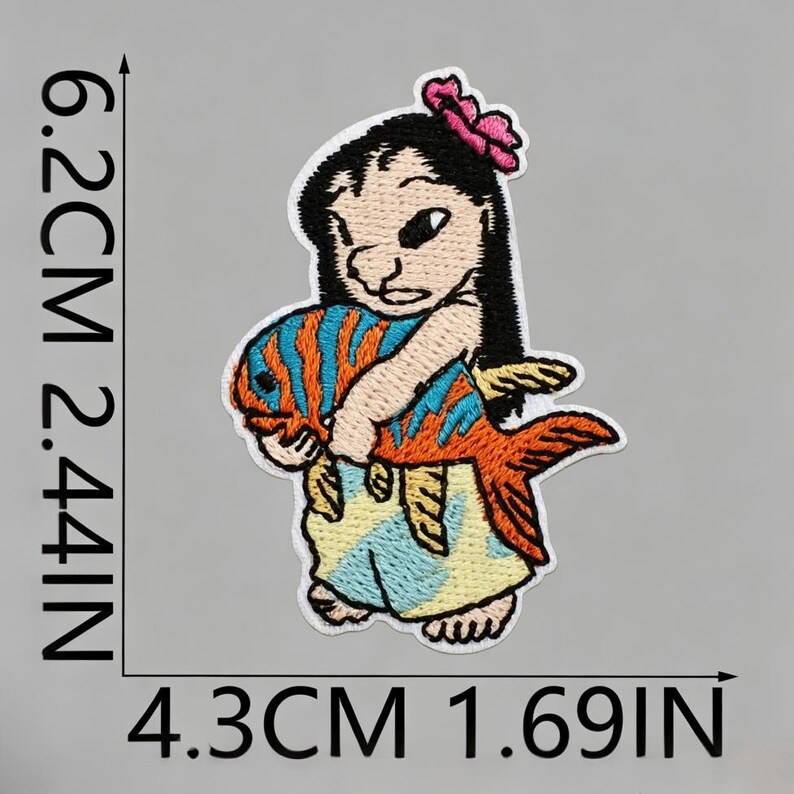 May include: An embroidered patch featuring a character with black hair and a pink flower, holding an orange and blue striped fish. The patch measures 6.2 cm by 4.3 cm, which is equivalent to 2.44 inches by 1.69 inches as indicated by the text.