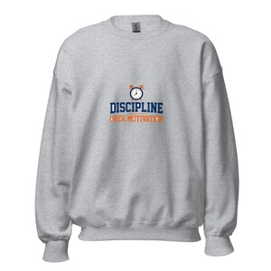 May include: A light gray crewneck sweatshirt featuring a graphic of a blue and orange alarm clock above the dark blue text DISCIPLINE and the orange text OVER MOTIVATION centered on the chest area of the garment.