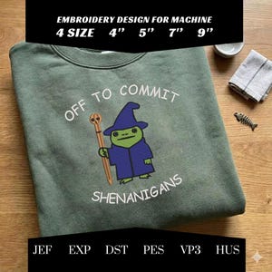 May include: Sage green sweatshirt with an embroidered design. The design features a cartoon frog in a wizard robe holding a staff, with the text "OFF TO COMMIT SHENANIGANS". The sweatshirt is available in 4", 5", 7", and 9" sizes.