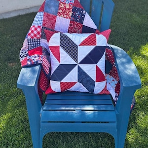 May include: A blue Adirondack chair on green grass holds a patchwork quilt and pillow. The quilt features red, white, and blue fabrics in various patterns. The pillow has a starburst design in the same colors. Text on the chair reads "Quilt sold separately."