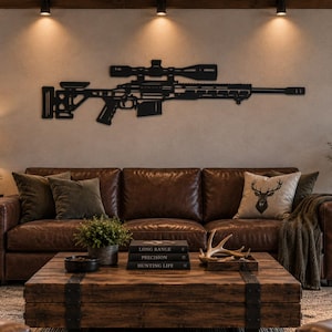 Op de afbeelding: Een wanddecoratie van zwart metaal in de vorm van een sluipschuttersgeweer met een vizier, een tactische kolf en een magazijn. Het silhouet is horizontaal bevestigd aan een lichte muur boven een bruine leren bank in een woonkamer.