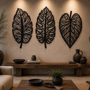 Puede incluir: Tres esculturas de pared negras con forma de hoja y patrones de venas recortados. Cada pieza presenta una forma botánica distinta, incluyendo una hoja alargada tipo pluma, una hoja dentada y un diseño de hoja en forma de corazón.