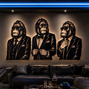 Puede incluir: Una gran pieza de arte mural de metal que muestra tres simios estilizados vestidos con trajes negros formales y corbatas, dos de ellos con gafas de sol. Las figuras están retroiluminadas, creando un efecto de silueta brillante en la pared gris.