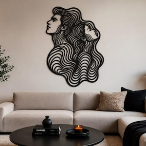 May include: A black metal wall art piece featuring the side profiles of two faces with long, flowing, wavy hair that merges into a singular, abstract, swirling pattern. The design is composed of continuous, interconnected lines.