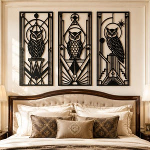 May include: Three black metal owl wall art panels in an Art Deco style. Each panel features a different owl design within geometric shapes. The panels are mounted above a bed with a beige headboard and pillows, creating a decorative bedroom scene.