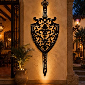 May include: A large, black, wall-mounted metal sculpture shaped like a sword and shield. The design features intricate, symmetrical scrollwork and floral patterns throughout the blade and shield area, with a fleur-de-lis motif at the hilt.