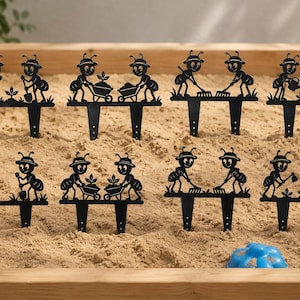 May include: A set of eight black metal garden stakes featuring silhouettes of cartoon ants performing various gardening tasks like digging, raking, and watering plants. Each stake has two pointed prongs at the base for insertion into soil.