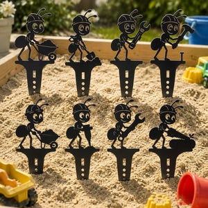 May include: A set of eight black metal garden stakes, each featuring a silhouette of an ant wearing a hard hat and performing construction tasks such as using a wheelbarrow, shovel, wrench, hammer, jackhammer, or saw, with a pointed base for soil.
