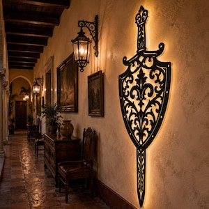 Puede incluir: Un aplique de pared de metal negro con forma de espada y un intrincado patr&oacute;n de filigrana. El dise&ntilde;o presenta una hoja puntiaguda y una guarda, con luz c&aacute;lida que emana desde detr&aacute;s del marco de metal, proyectando un brillo en la pared.