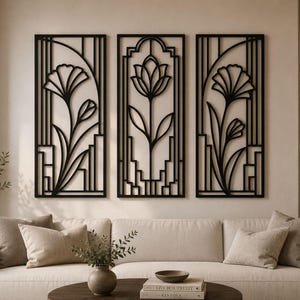 May include: Three black metal wall art panels with floral designs. Each panel features a different stylized flower, with stems and leaves. The panels are rectangular and mounted on a beige wall above a cream-colored sofa.