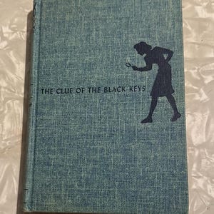 May include: A white ceramic mug with a black handle and the text "But First, Coffee" in a bold, black font. The mug is set against a blurred background, suggesting a cozy setting.