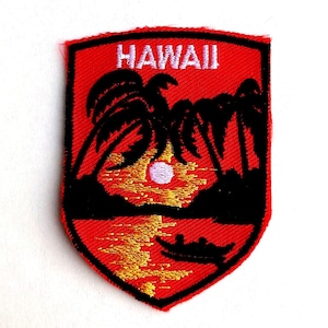 May include: A shield-shaped embroidered patch with a red background featuring a black silhouette of palm trees, a small boat, and a sunset over water. The word HAWAII is stitched in white capital letters at the top of the patch.