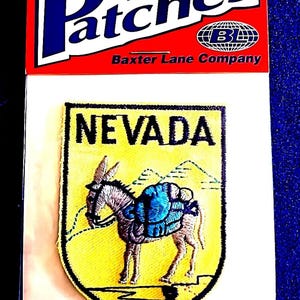 May include: Iron-on patch featuring a yellow shield with a donkey carrying a pack, the word "NEVADA" above. The patch is bordered in black and set against a white background, with a red and white header that reads "Patches".