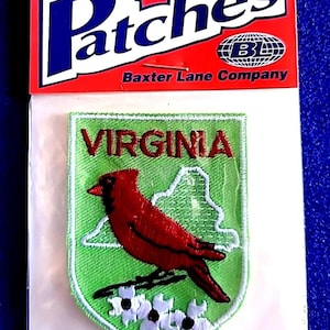 May include: Iron-on patch featuring a red cardinal bird, the state name "VIRGINIA", and a state outline on a green background. The patch is in a clear plastic package with a red header that says "Patches" and "Baxter Lane Company".