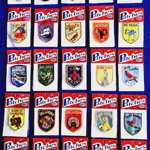 May include: A collection of twenty-five embroidered state souvenir patches, each mounted on a white card labeled Patches. The patches feature various state names, symbols, and illustrations, including animals, landmarks, and floral designs in colors.
