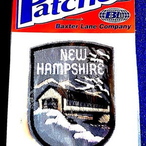 May include: Iron-on patch featuring a detailed embroidered design of a covered bridge and mountains, with the text "NEW HAMPSHIRE". The patch is on a white backing with a red and blue header that reads "Patches" and "Baxter Lane Company".