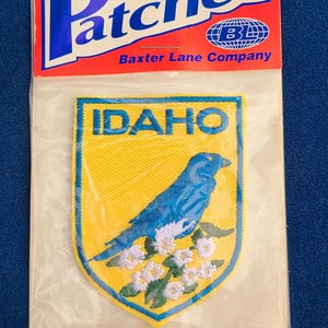 May include: An iron-on patch featuring the word "Patches" in blue and white, with the Baxter Lane Company logo. The patch has a yellow background with a blue bird and the word "IDAHO".