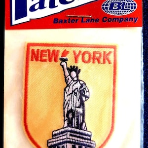 May include: A New York City patch featuring the Statue of Liberty, with the words "NEW YORK" in red. The patch is yellow with a red border and is packaged in a clear plastic bag. The packaging includes the word "Patches" in blue.